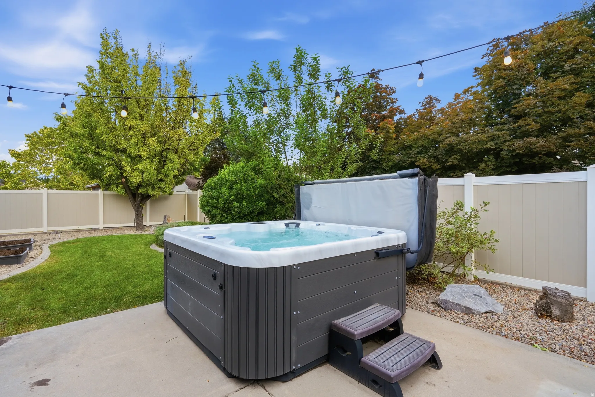 Outdoor spa with steps, concrete patio, gravel border, and privacy fencing