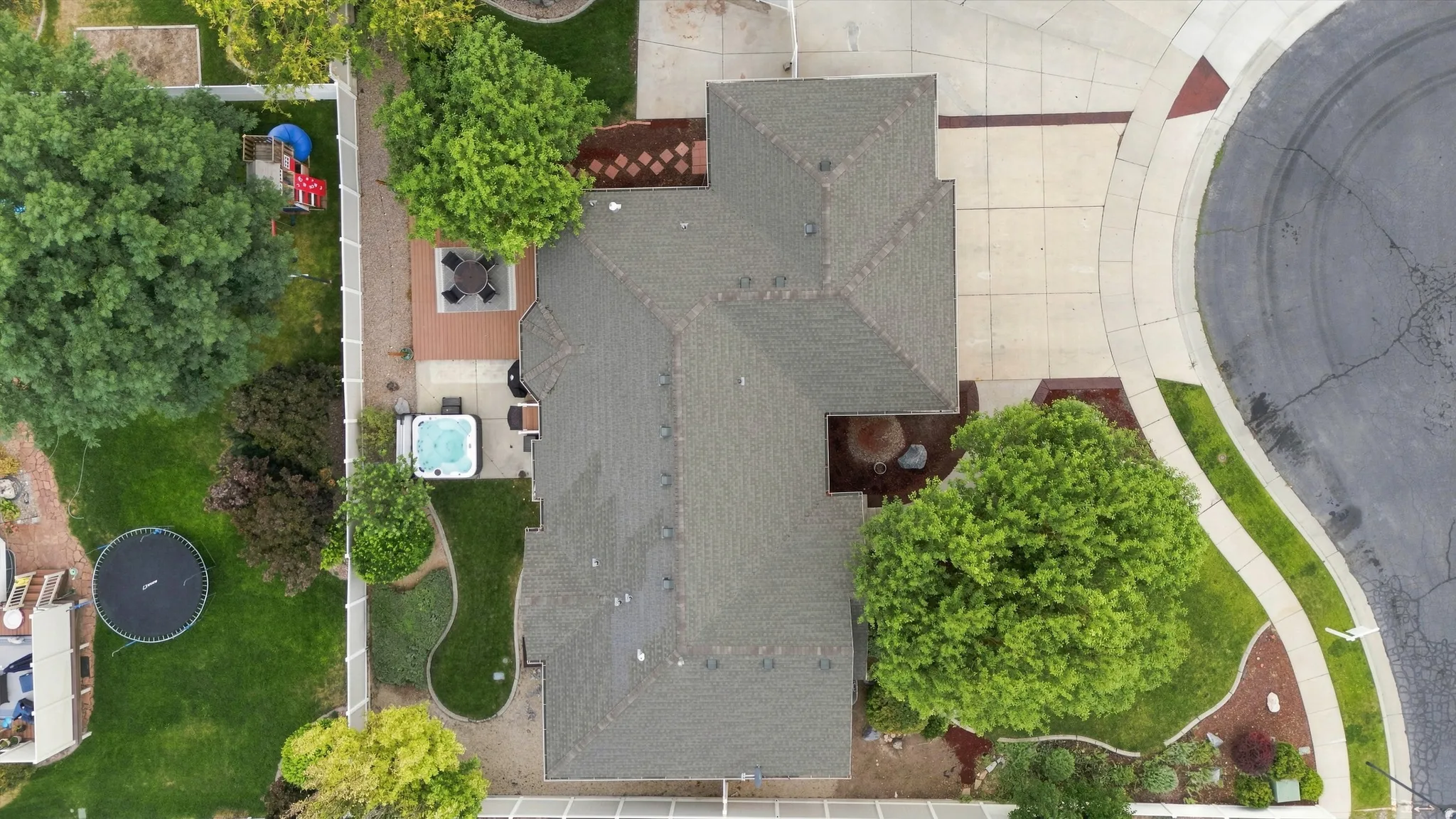 Aerial view showcasing a thoughtfully designed outdoor living space featuring mature landscaping, expansive lawn areas, a concrete patio, and integrated hardscaping elements
