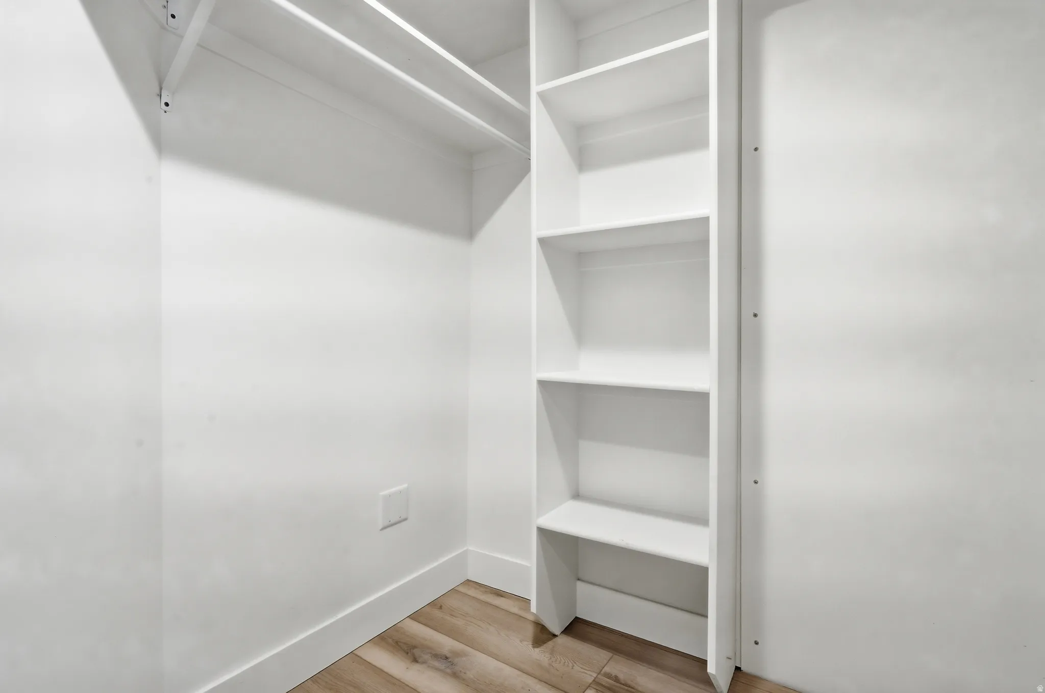 Built-in shelving, two closet rods, clean white walls, and wood-finish flooring