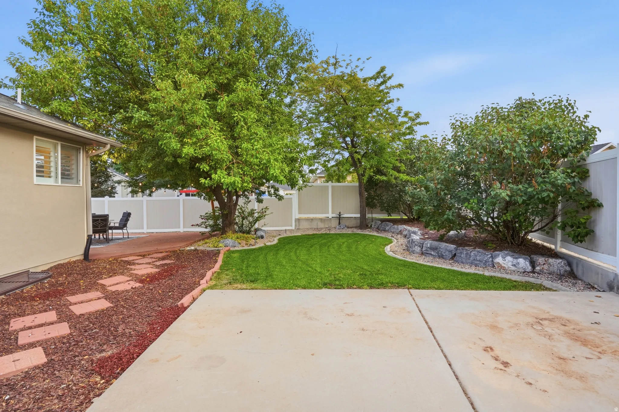 Spacious backyard oasis featuring a lush, manicured lawn, mature shade trees, and defined planting beds with decorative stone borders