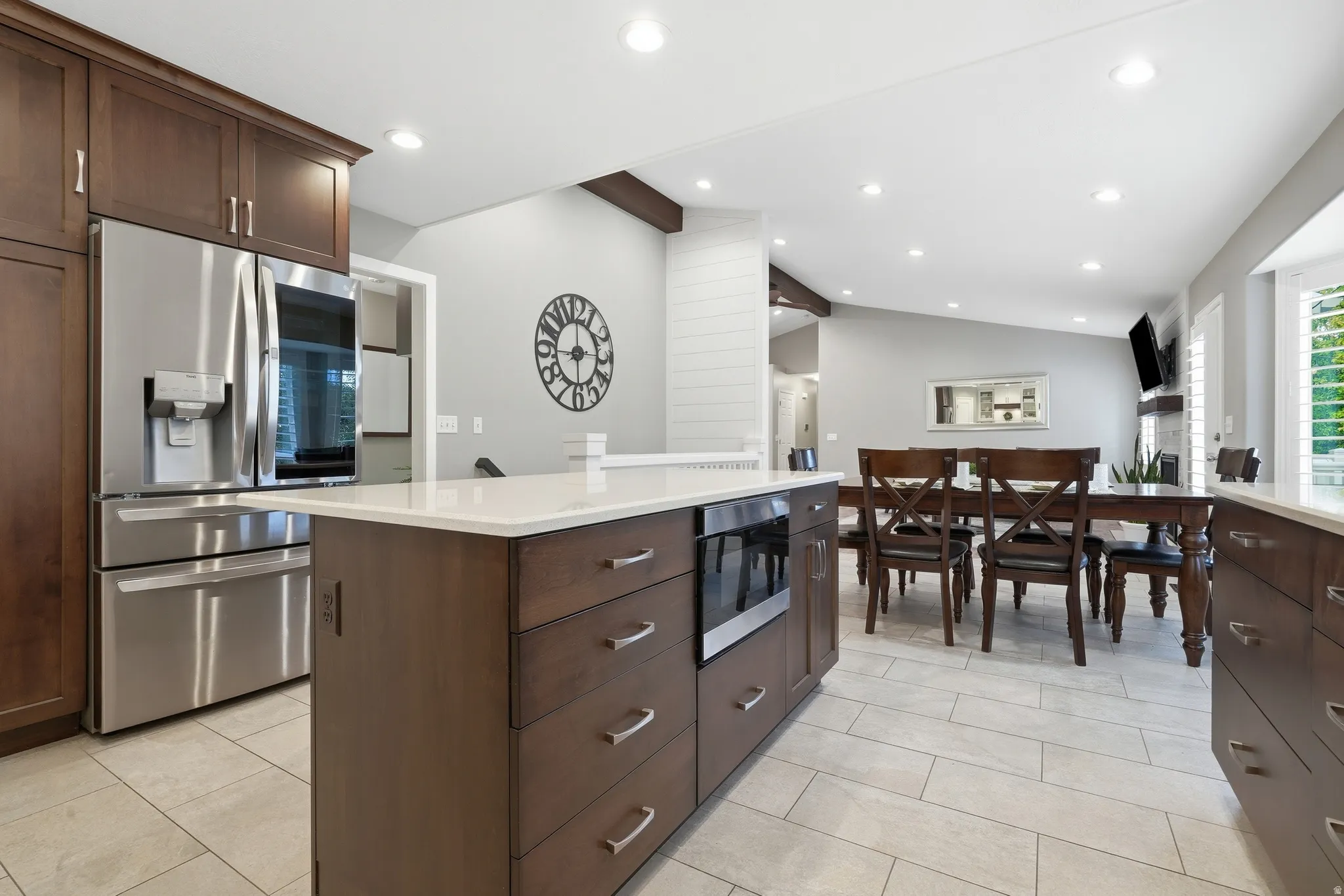 Central kitchen island with white countertop, recessed lighting, stainless steel appliances, dark wood-finish cabinetry, and light tile flooring