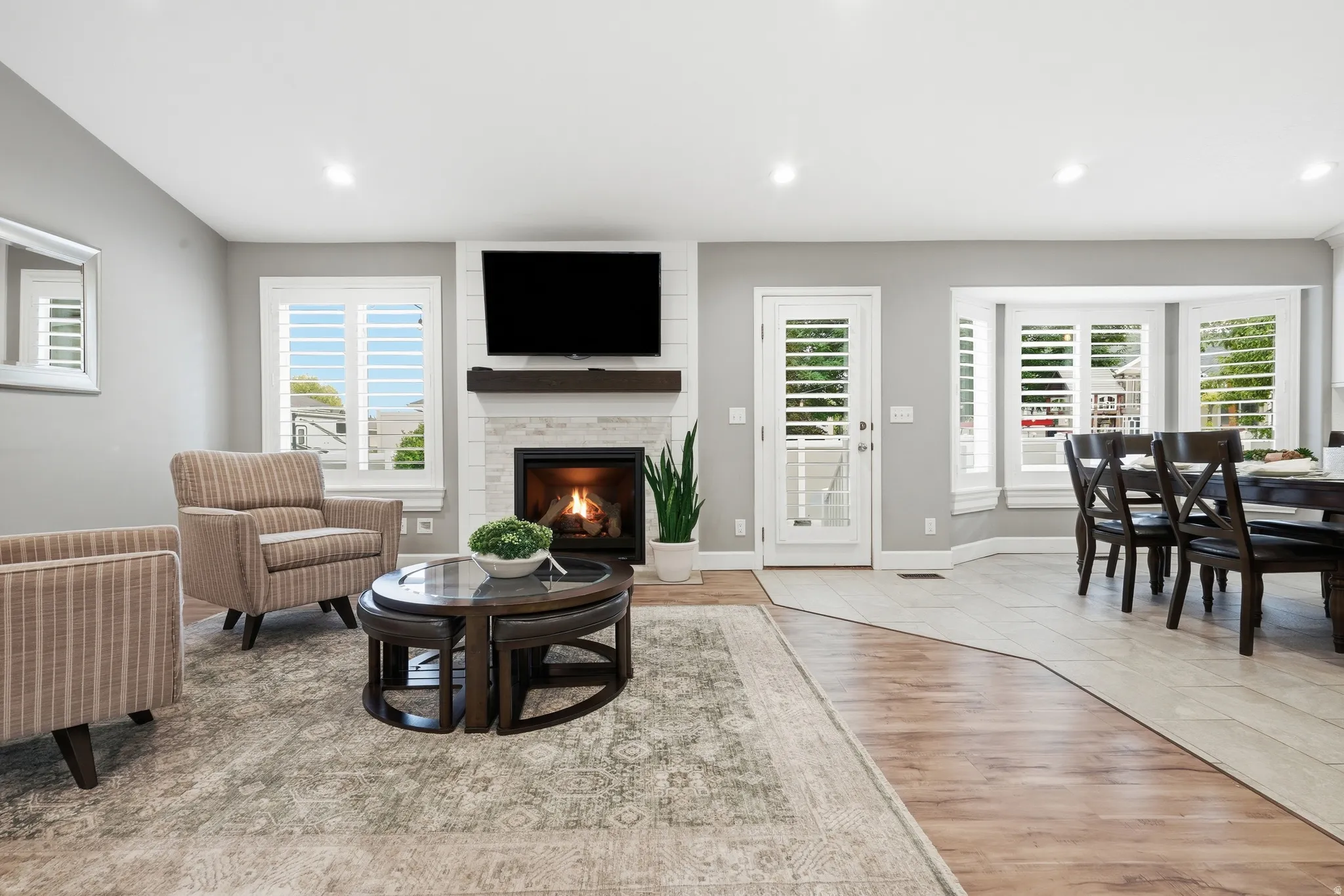 Open-concept living area featuring a gas fireplace with a mounted flat-screen television, recessed lighting throughout, and multiple sets of French doors with plantation shutters opening to outdoor spaces