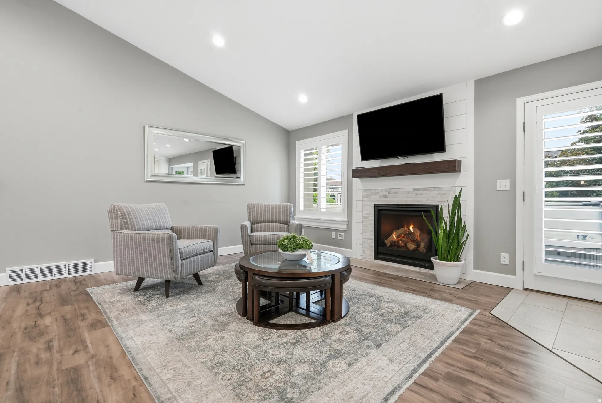 Vaulted ceiling, wood-finish flooring, recessed lighting, fireplace with stone surround and wood mantle, and white plantation shutters