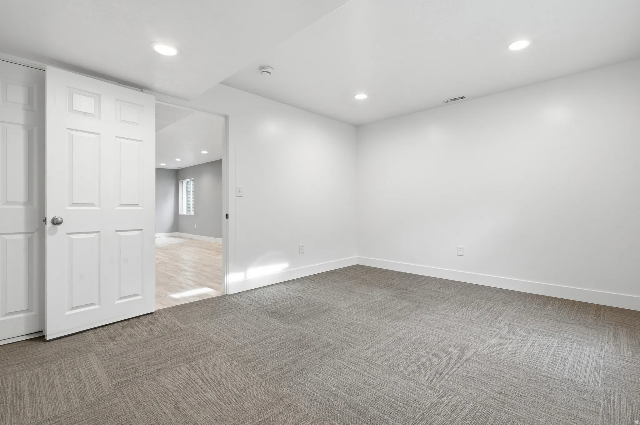 Spacious room featuring engineered wood-finish flooring in a herringbone pattern, recessed ceiling lighting, and pristine white walls
