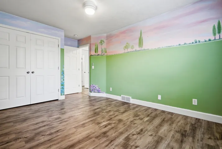 Spacious room featuring wood-finish flooring, fresh green accent walls with scenic mural detail, white six-panel closet doors, and multiple electrical outlets
