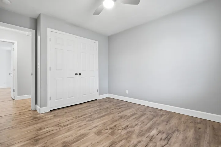 Wood-finish flooring, white panel bi-fold closet doors, ceiling fan with integrated lighting, and light gray wall paint