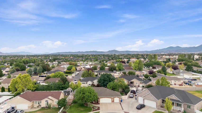 Aerial perspective showcasing this residential property situated in an established neighborhood with mature landscaping, tree-lined streets, and mountain vistas in the distance