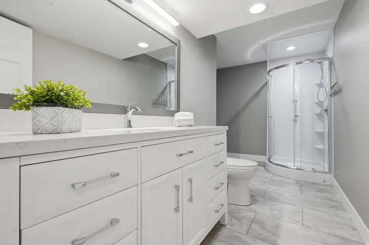 Bathroom featuring a curved glass shower enclosure, white vanity with ample storage, integrated sink, and a large wall-mounted mirror