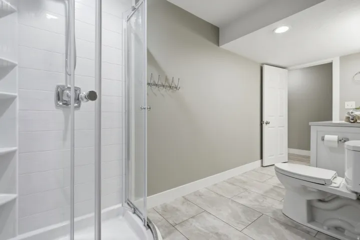 Modern primary bathroom featuring a frameless glass-enclosed shower with subway tile surround, dual vanity with white cabinetry and integrated sink, ceramic tile flooring, recessed lighting, and neutral wall finishes