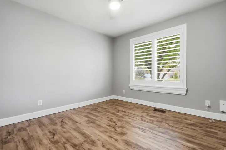 Bright bedroom showcasing wood-finish flooring, neutral gray walls, and white trim throughout