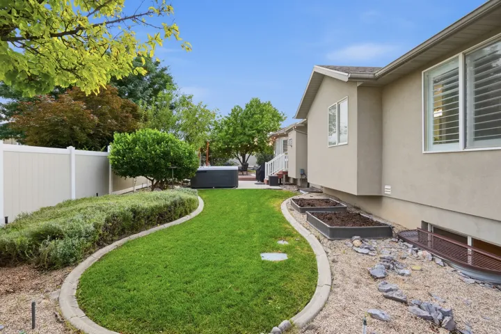 Expansive backyard oasis featuring a meticulously manicured lawn bordered by curved concrete hardscaping, mature landscaping with established trees, and low-maintenance planting beds