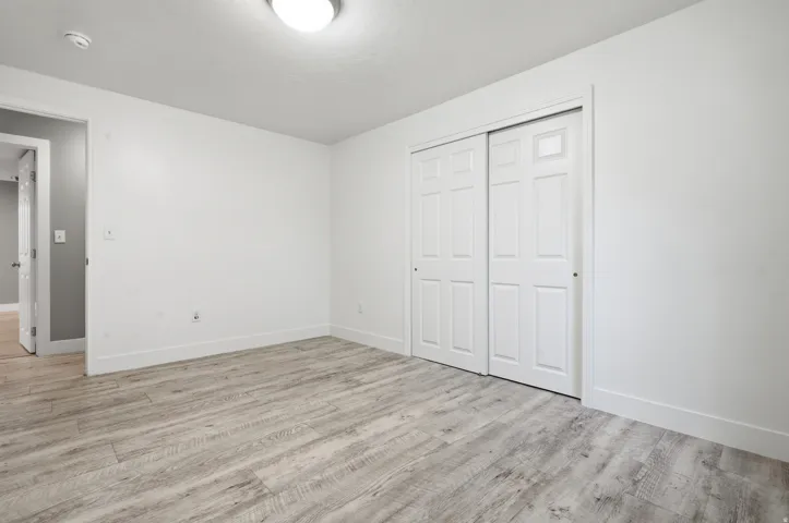 Neutral-toned wood-finish flooring, white walls, white trim, and a white bi-fold closet