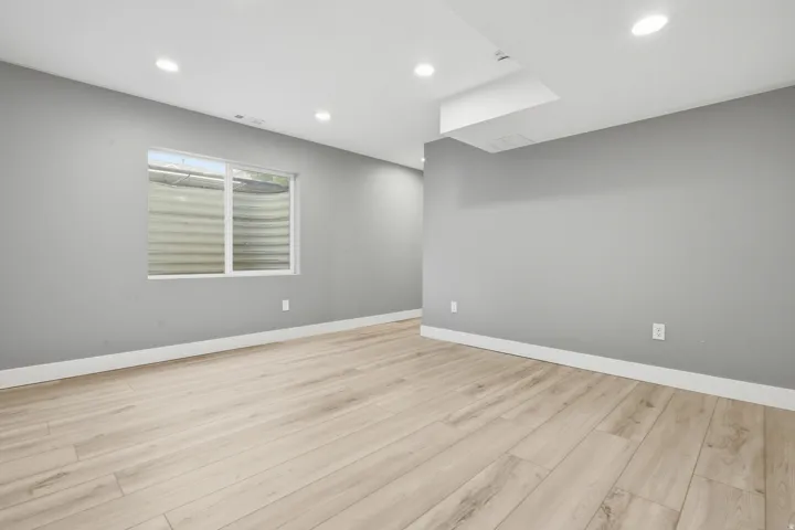 Spacious room featuring light wood-finish flooring, gray painted walls, recessed ceiling lighting, and a skylight providing natural illumination