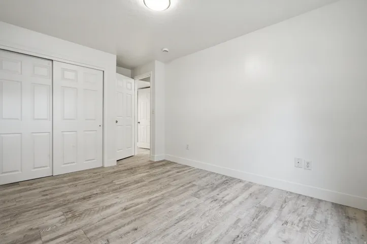 Spacious bedroom featuring wood-finish flooring, dual closets with six-panel doors, recessed ceiling lighting, and clean white walls with electrical outlets