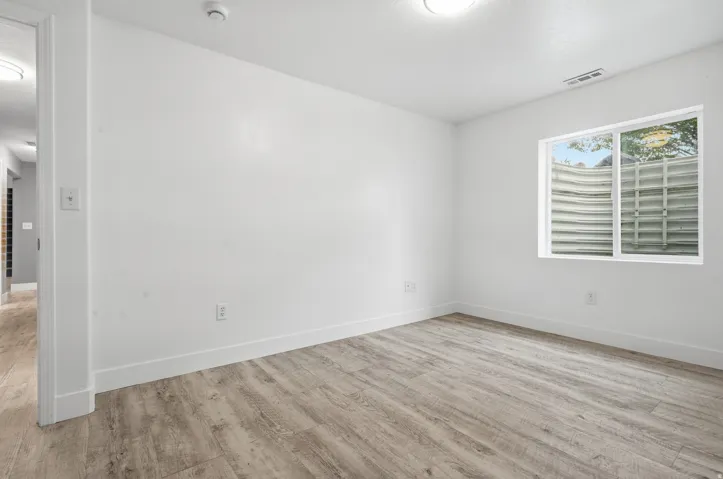 Bright, light-filled room with expansive wood-finish flooring, recessed ceiling lighting, and large windows with operable shutters providing natural illumination and ventilation control