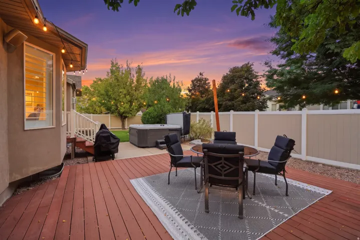 Expansive wood deck with string lighting, hot tub, and fenced perimeter