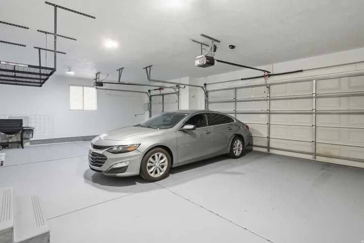 Dual garage doors, overhead storage racks, light-colored flooring, window, and automated garage door openers