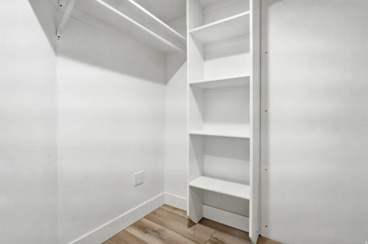 Built-in shelving, two closet rods, clean white walls, and wood-finish flooring
