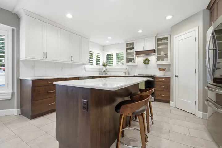 Gourmet kitchen featuring white cabinetry with glass-front upper cabinets, a two-tone island with waterfall countertop and seating for multiple, stainless steel appliances, tile flooring, and abundant recessed lighting throughout the space