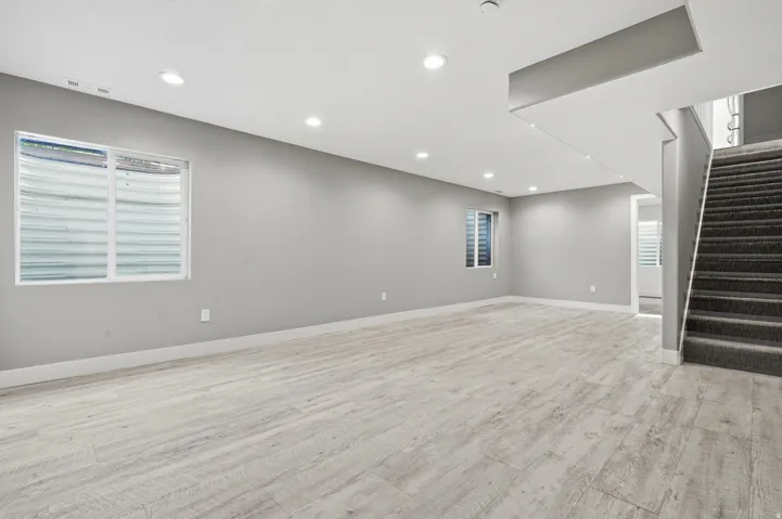 Spacious open room featuring light wood-finish flooring, recessed ceiling lighting, and expansive windows with plantation shutters