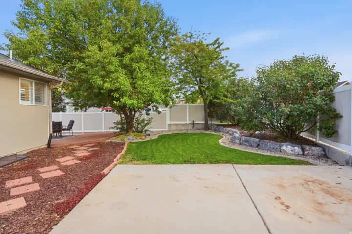 Spacious backyard oasis featuring a lush, manicured lawn, mature shade trees, and defined planting beds with decorative stone borders