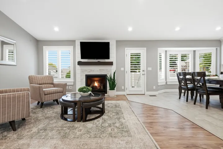 Open-concept living area featuring a gas fireplace with a mounted flat-screen television, recessed lighting throughout, and multiple sets of French doors with plantation shutters opening to outdoor spaces