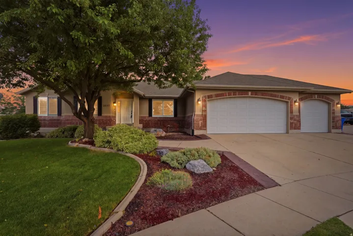 Stunning brick and stone residence showcasing a two-car garage, mature landscaping with curved hardscape borders, and professional outdoor lighting