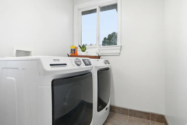 White appliances featuring a front-load washer and dryer, tile flooring, and a single window