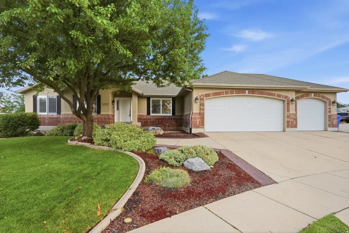 Charming brick ranch home showcasing a mature shade tree, manicured lawn with curved landscaping borders, decorative mulch beds, and a two-car garage with architectural detailing