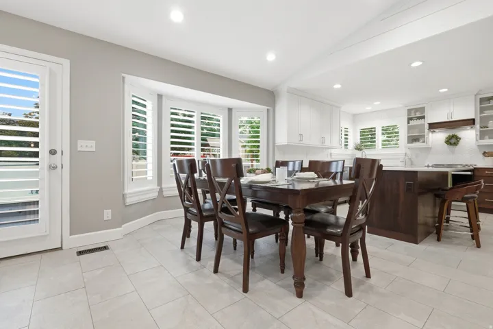 Spacious dining area with bay windows, white plantation shutters, and light-toned tile flooring