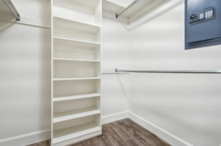 Spacious walk-in closet featuring extensive built-in shelving with multiple compartments, a hanging rod for garment storage, wood-finish flooring, and a wall-mounted safe for secure valuables storage