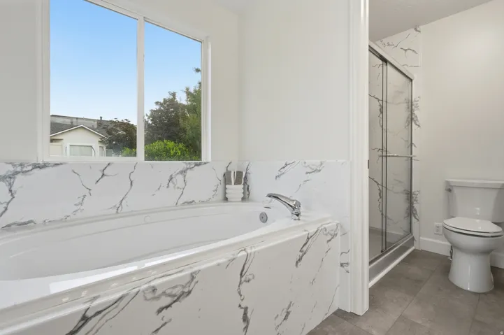 Spa-inspired primary bathroom featuring a marble-look tile surround, soaking tub with chrome fixtures, walk-in shower with frameless glass enclosure, and dual vanity
