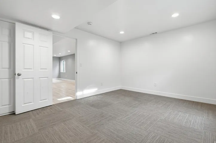 Spacious room featuring engineered wood-finish flooring in a herringbone pattern, recessed ceiling lighting, and pristine white walls