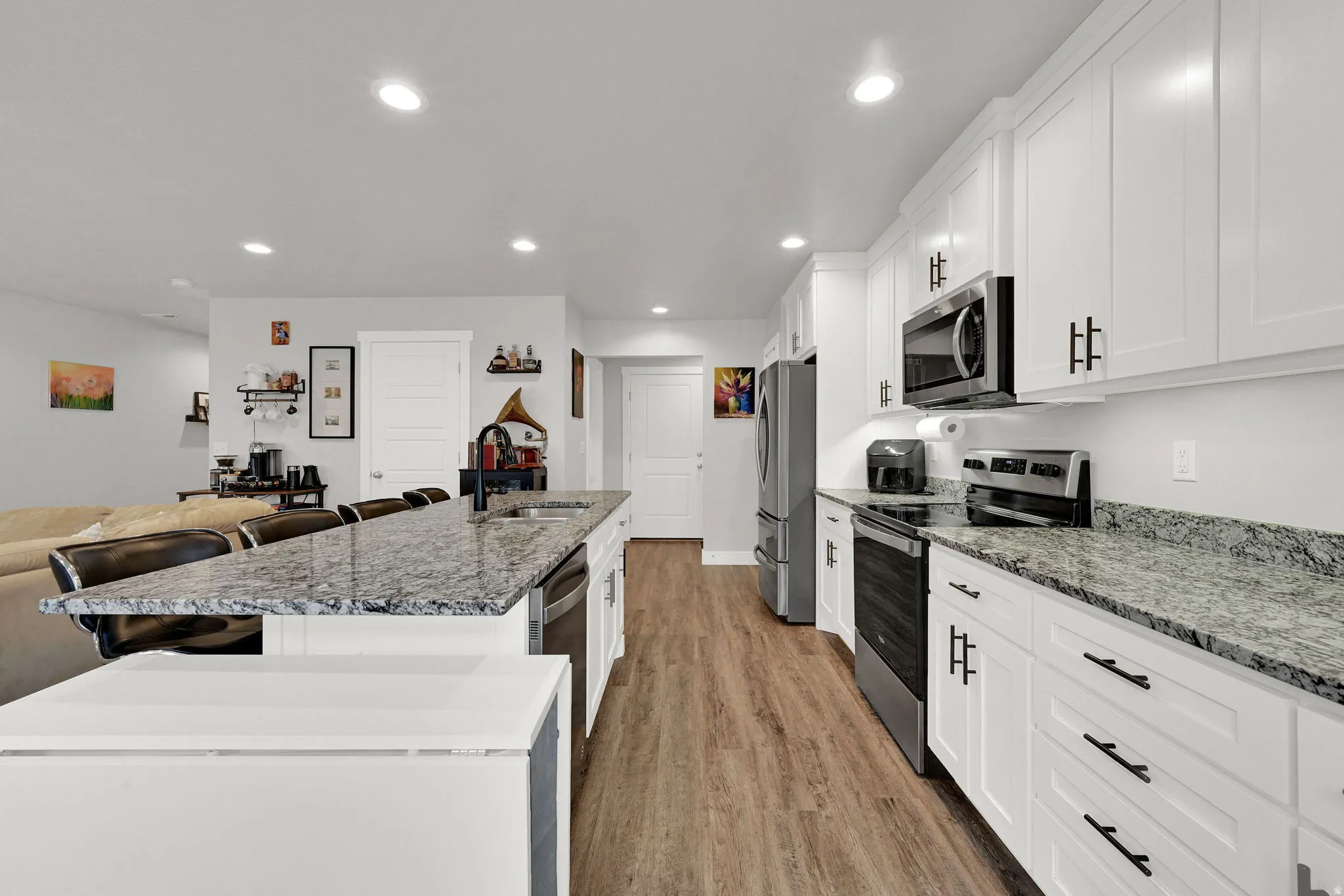 Kitchen featuring white cabinetry, dark hardware, stainless steel appliances, granite countertops, and LVP wood-finish flooring
