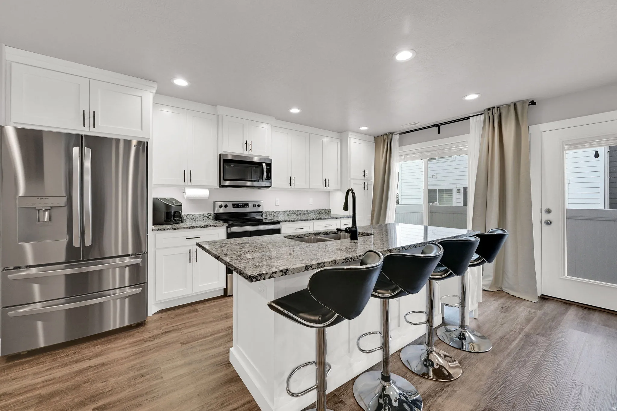 White cabinetry, LVP wood-finish flooring, stainless steel appliances, granite countertops, and a kitchen island with seating