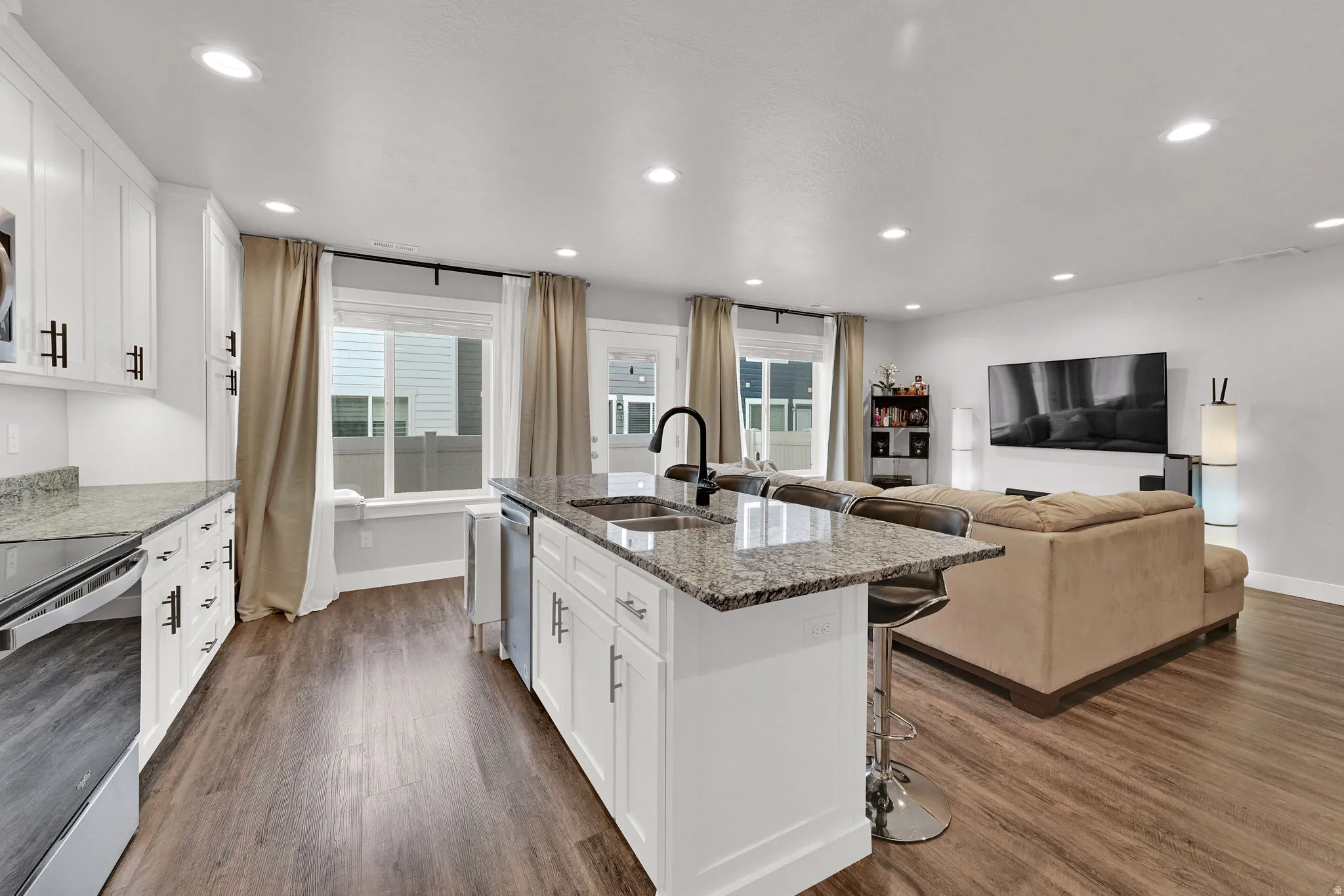 Open-concept kitchen and living area featuring white cabinetry with hardware accents, a large island with waterfall-edge countertop and seating, stainless steel appliances, and recessed ceiling lighting