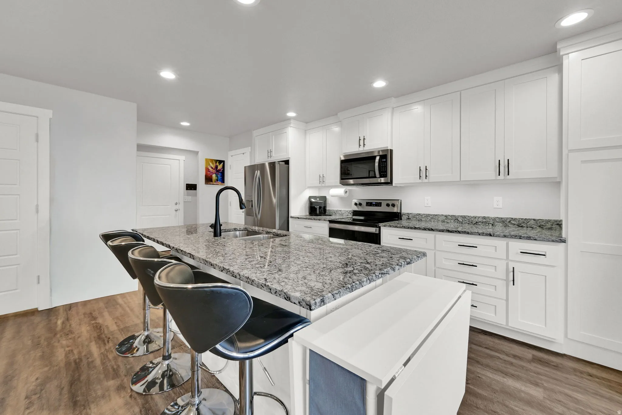 Modern kitchen featuring white shaker-style cabinetry, stainless steel appliances, and a large granite-topped island with seating for multiple guests