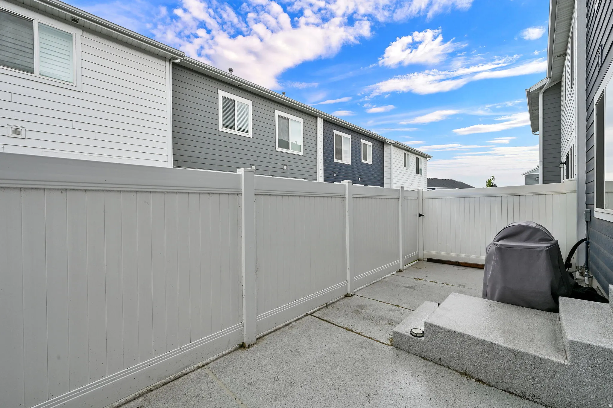 Private concrete patio featuring a white privacy fence and exterior siding