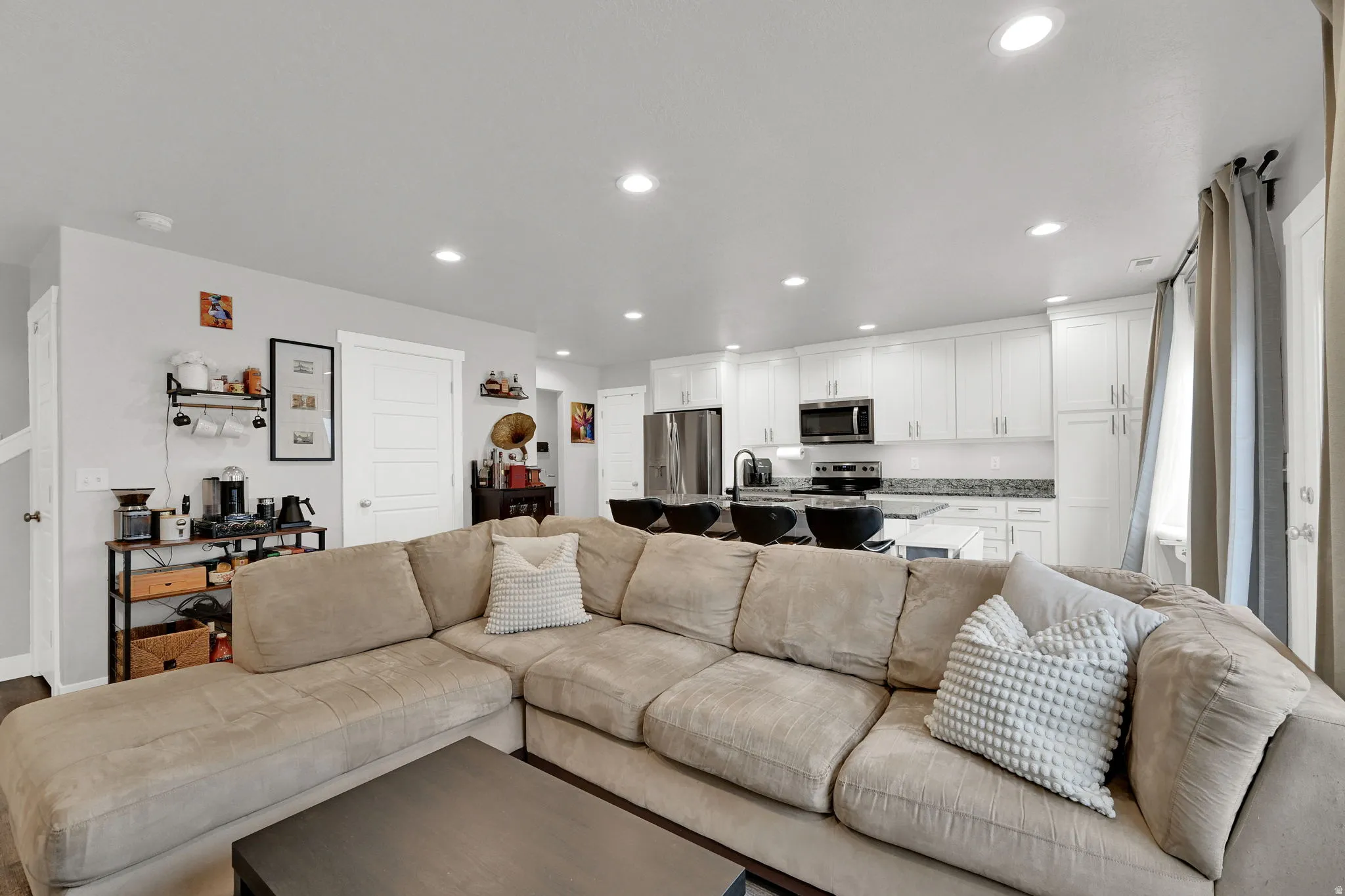 Open-concept living area featuring recessed lighting, white perimeter cabinetry, stainless steel appliances, and a kitchen island with seating