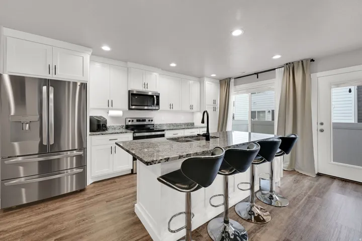 White cabinetry, LVP wood-finish flooring, stainless steel appliances, granite countertops, and a kitchen island with seating
