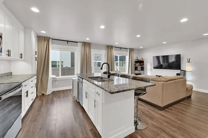 Open-concept kitchen and living area featuring white cabinetry with hardware accents, a large island with waterfall-edge countertop and seating, stainless steel appliances, and recessed ceiling lighting