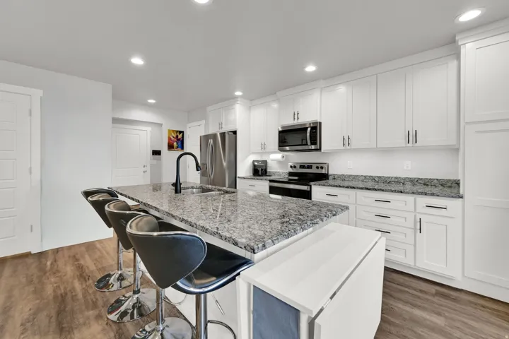 Modern kitchen featuring white shaker-style cabinetry, stainless steel appliances, and a large granite-topped island with seating for multiple guests