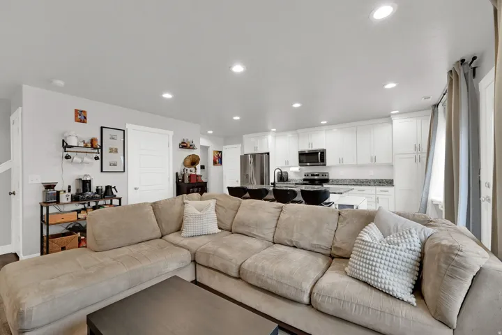Open-concept living area featuring recessed lighting, white perimeter cabinetry, stainless steel appliances, and a kitchen island with seating