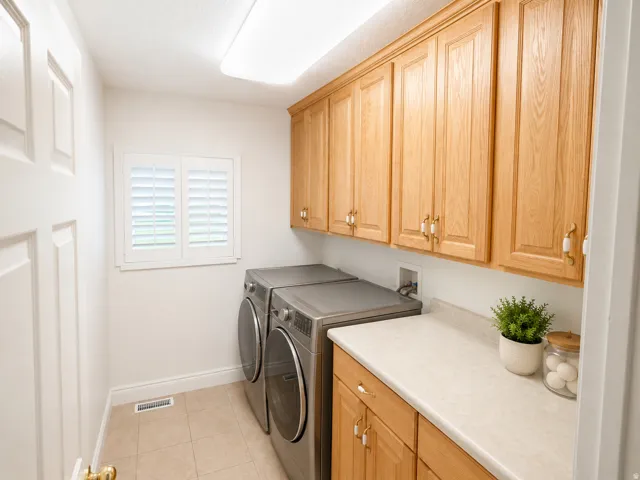 Laundry area featuring wood cabinetry, a light-toned countertop, and a window with plantation shutters