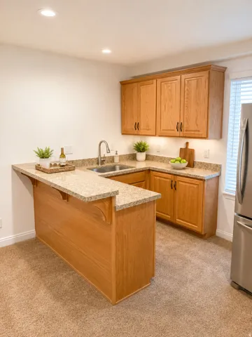 Corner kitchen area featuring wood cabinetry, speckled countertops, a stainless steel sink, and recessed lighting