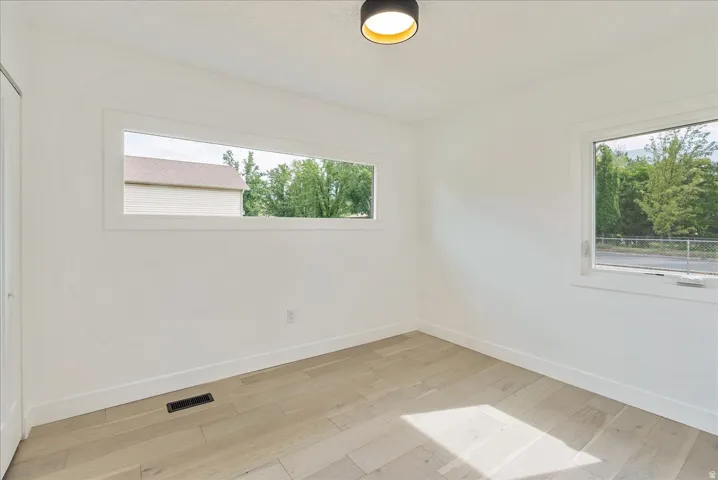 Bright, light-filled bedroom showcasing wood-finish flooring, expansive windows with natural light, and clean white walls