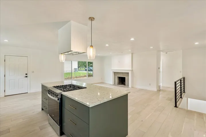 Open-concept living space featuring wood-finish flooring, a kitchen island with a built-in range, pendant lighting, recessed lighting, and a fireplace with a Tile surround