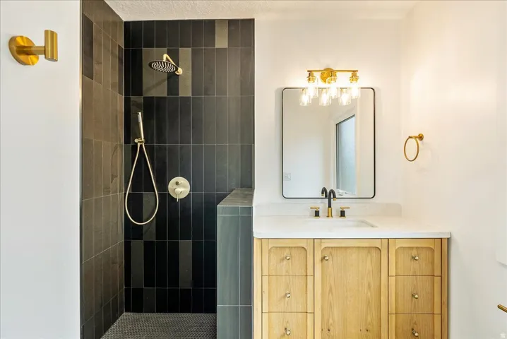 Contemporary bathroom featuring a custom wood-finish vanity with multiple drawers and brass hardware, white quartz countertop, and a rectangular framed mirror with brass accents