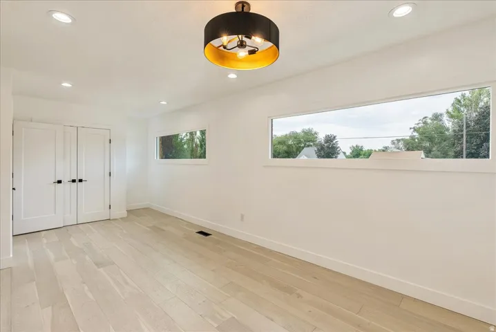 Bright, open room featuring light wood-finish flooring throughout, expansive windows framing natural scenery, recessed ceiling lighting, and a contemporary black and brass pendant fixture