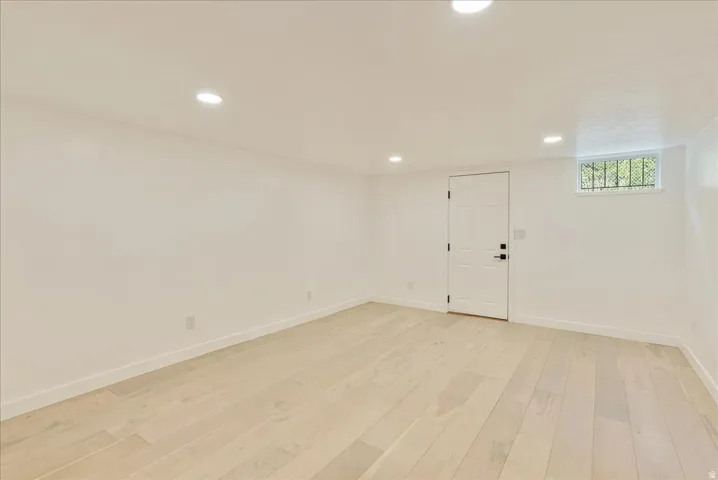 Bright, freshly finished basement space with recessed lighting throughout, light wood-finish flooring, and white wall